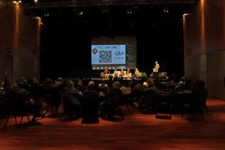 A group of people sitting in chairs in front of a large screen

Description automatically generated