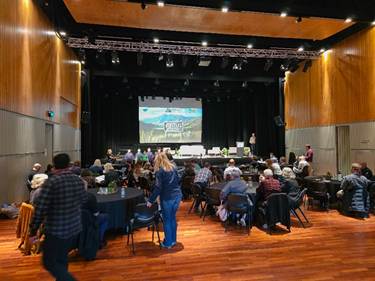 A group of people sitting in chairs in a room with a projector screen

Description automatically generated