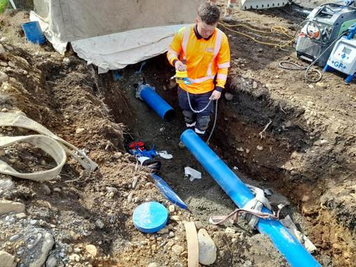 A person in a yellow vest working on a pipe

Description automatically generated